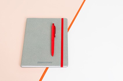 Szary notes w twardej oprawie z czerwoną gumką i długopisem